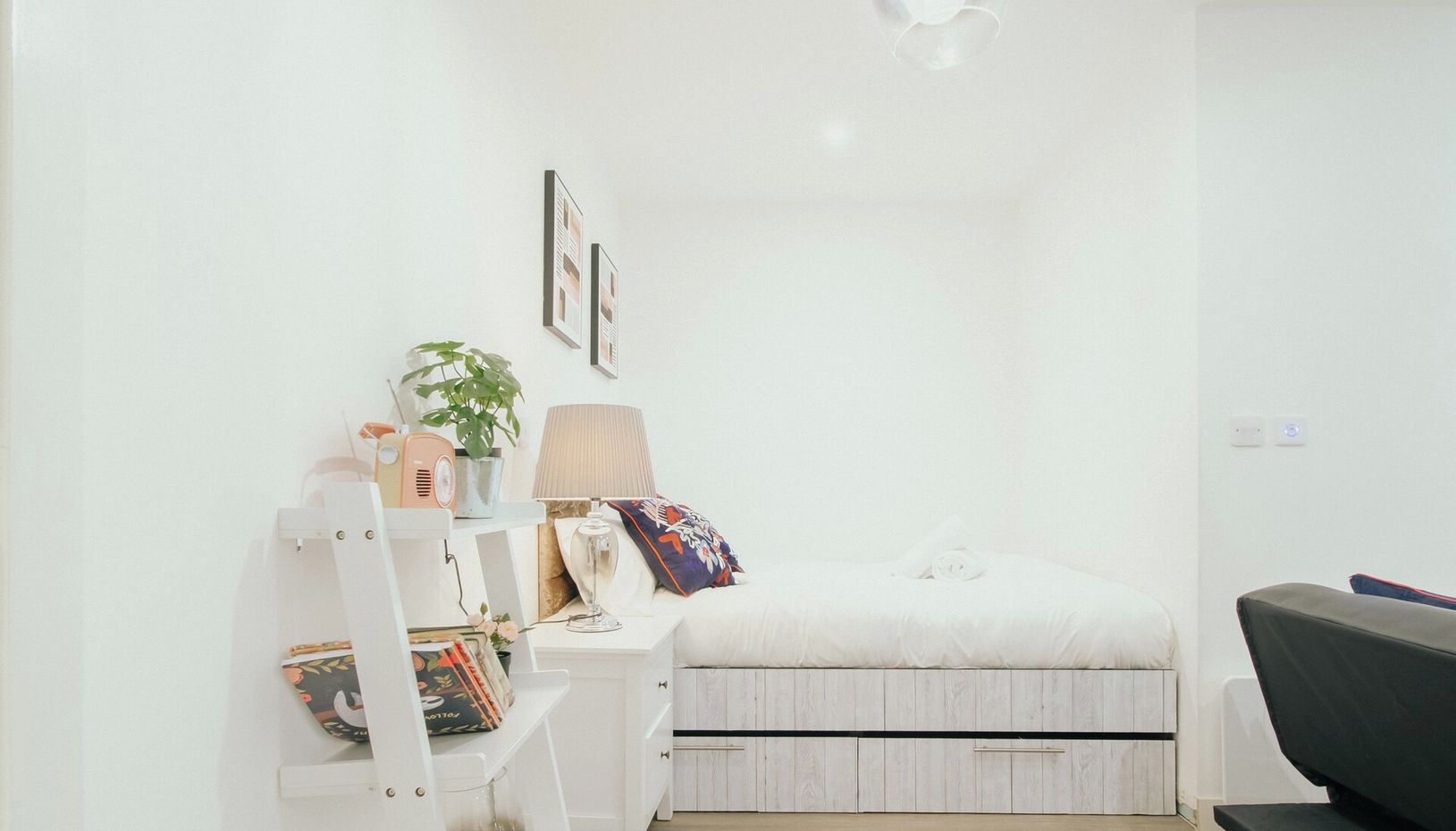 A modern bedroom with a bed, bedside table, lamp, and a small plant.