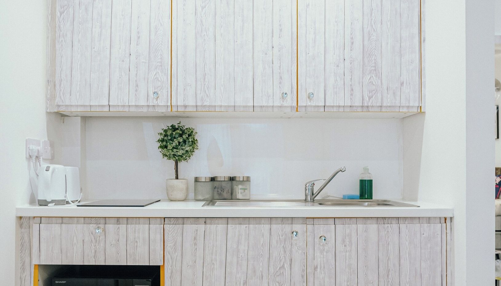 A modern kitchen with wooden cabinets, a built-in microwave, a small potted plant, and a sink with a faucet.