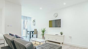 En moderne stue med sofa, spisebord og fjernsyn ophængt på væggen.