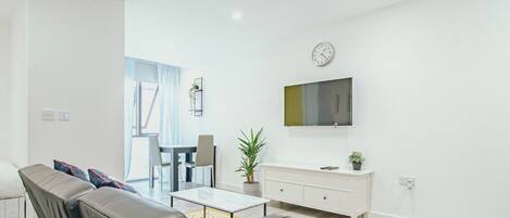 Un salon moderne avec un canapé, une table à manger et un téléviseur fixé au mur.