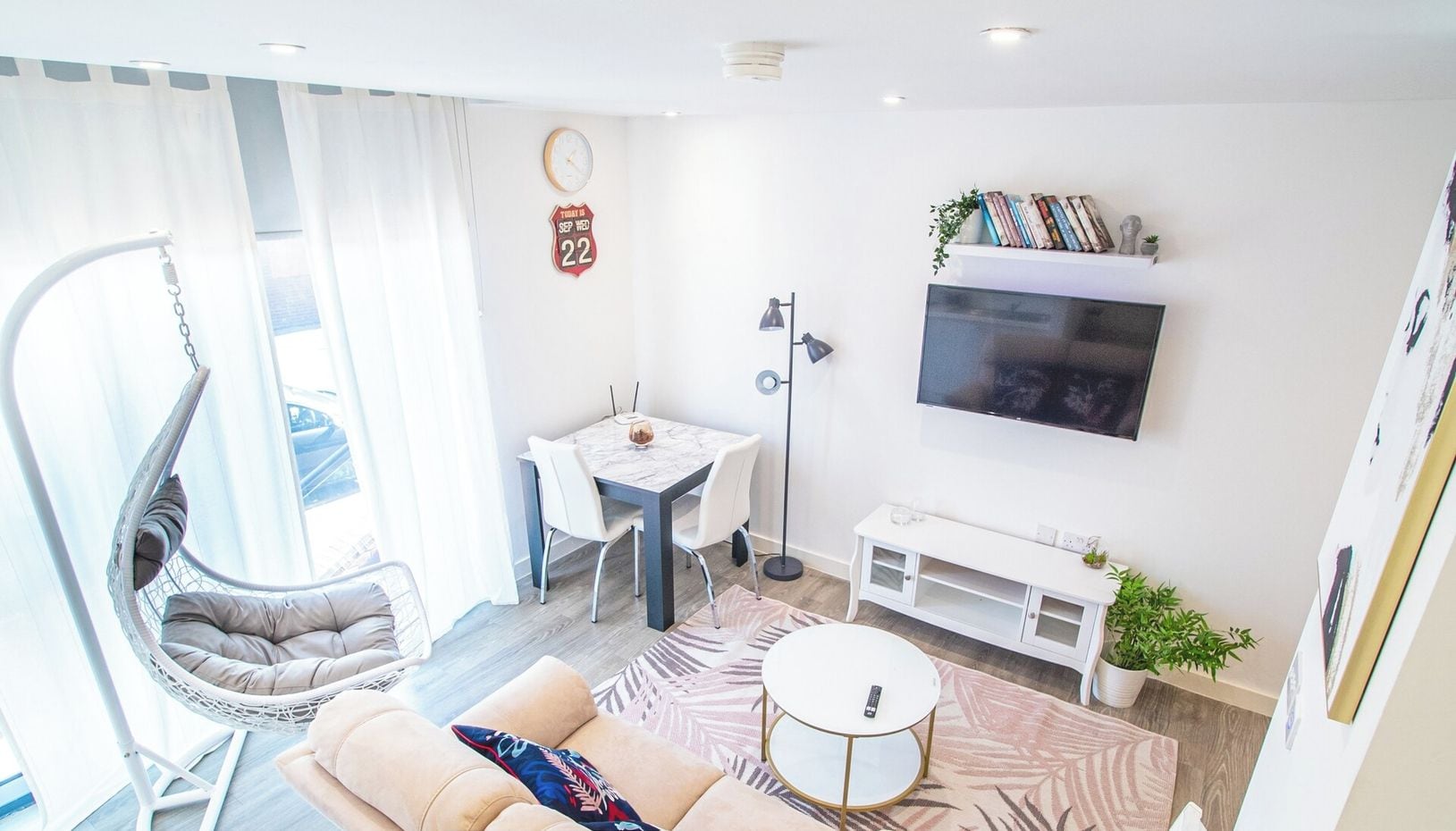 A modern living room with a sofa, a hanging chair, a dining table, and a TV.