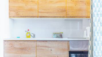 A kitchen with wooden cabinets, a white countertop, a sink, and a microwave. There are jars on the counter and a dish soap bottle.