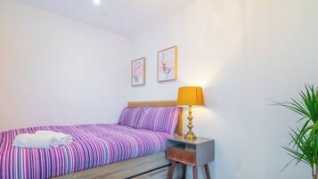 A bedroom with a bed, a nightstand, a lamp, and a potted plant.