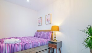 A bedroom with a bed, a nightstand, a lamp, and a potted plant.