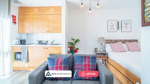 Een modern appartement met keuken, een eethoek, een woonkamer met een bank en een slaapkamer met een bed en nachtkastje.