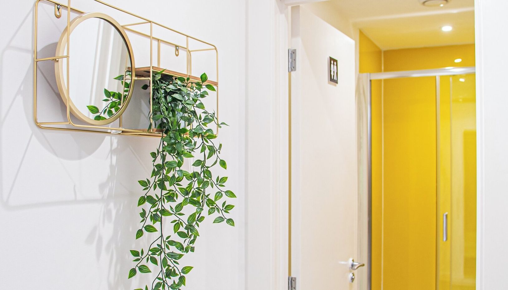 Et vægmonteret spejl med en hængende plante, en gul dør og et skilt for AVO APARTMENTS og Airbnb.