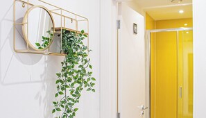 A wall-mounted mirror with a hanging plant, a yellow door, and a sign for AVO APARTMENTS and Airbnb. - Retro Ground Floor Studio in Sheffield – APT 14 (Sheffield)