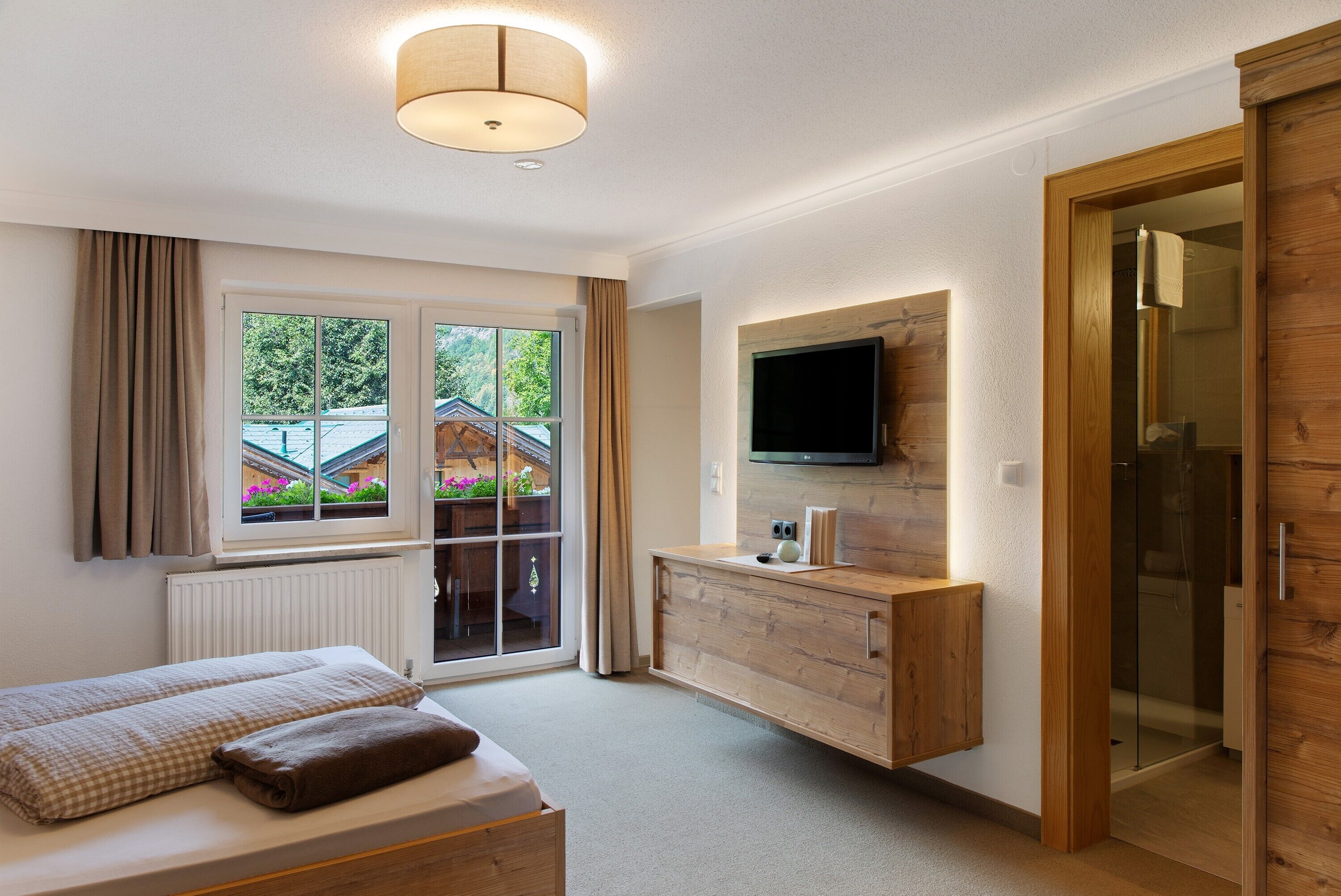 Ein Schlafzimmer mit einem Bett, einem an der Wand montierten Fernseher, einem Holzschrank und einer Glastür zum Balkon.