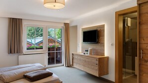 A bedroom with a bed, a TV mounted on the wall, a wooden cabinet, and a sliding glass door leading to a balcony.