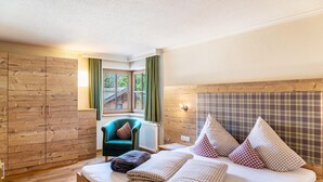 A bedroom with a wooden headboard, a bed with checkered bedding, a green armchair, and a window with curtains.