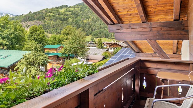 A wooden balcony with a view of a mountainous landscape, a chair, and a table.