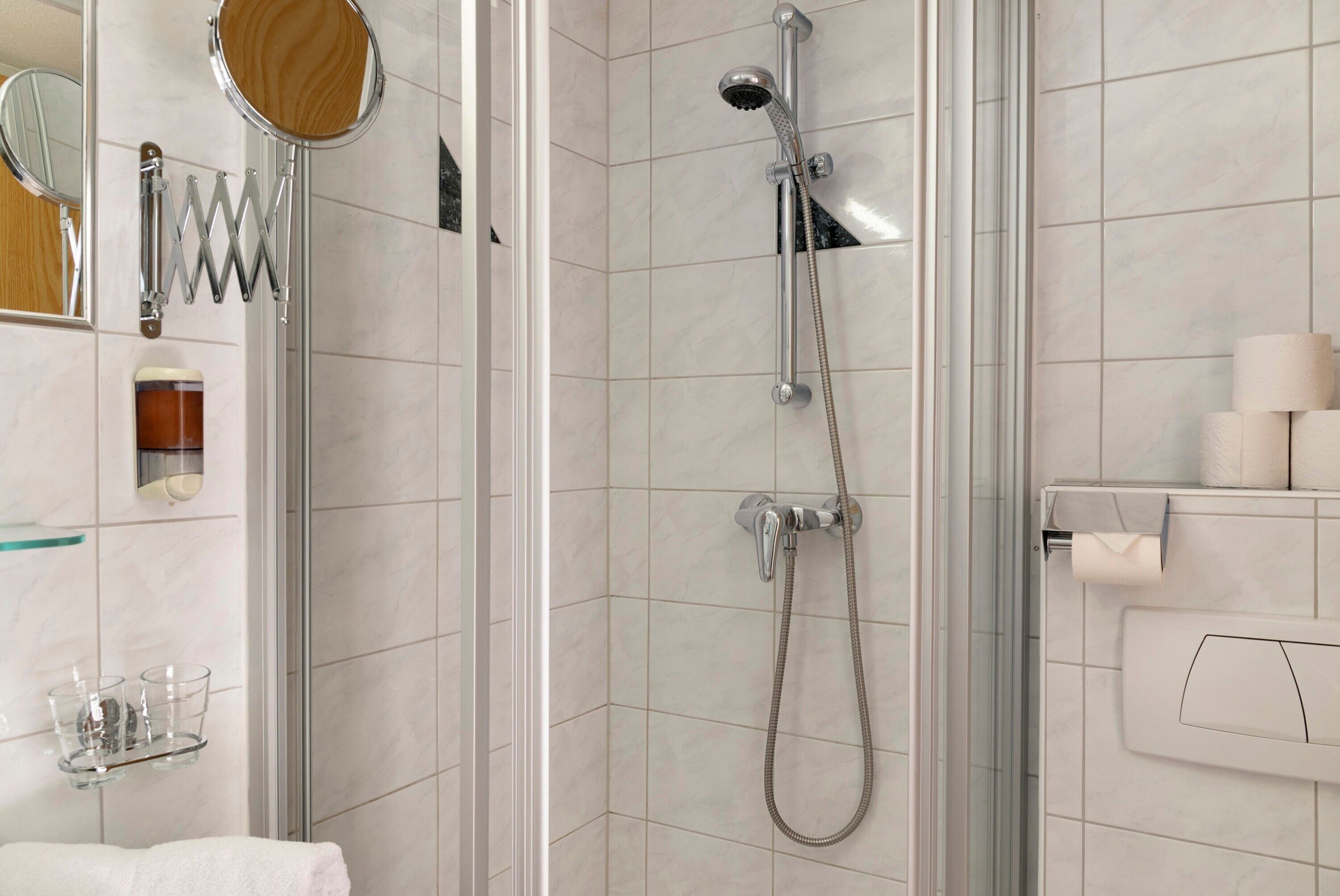 A modern bathroom with a glass shower enclosure, a handheld showerhead, a towel rack, and a toilet paper holder.