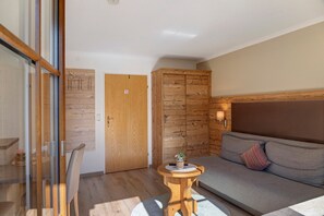A modern room with a wooden door, a sofa with cushions, a small round table with a plant, and a glass partition. - Apartment 'Top 5' with Mountain View, Balcony and Wi-Fi (Oetz)