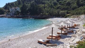 A beach with wooden lounge chairs and umbrellas, rocky shoreline, and a building in the background.