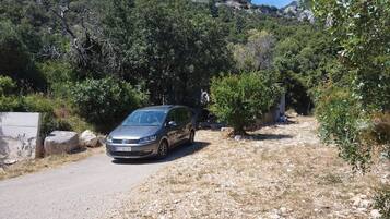 Une voiture est garée sur un chemin de gravier, avec une chaîne de montagnes en arrière-plan.