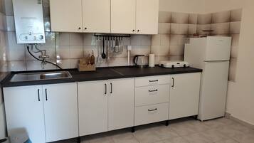 A kitchen with white cabinets, a black countertop, a stainless steel sink, a kettle, a coffee maker, and a refrigerator.
