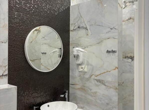 A bathroom with a marble vanity, a round mirror, a white sink, and a shower area with a handheld showerhead. - Rooms Lidija 32 (Zagreb)