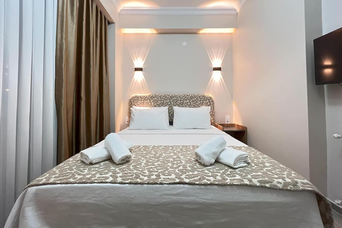 A hotel room with a bed, two bedside lamps, a TV, and a window with curtains.