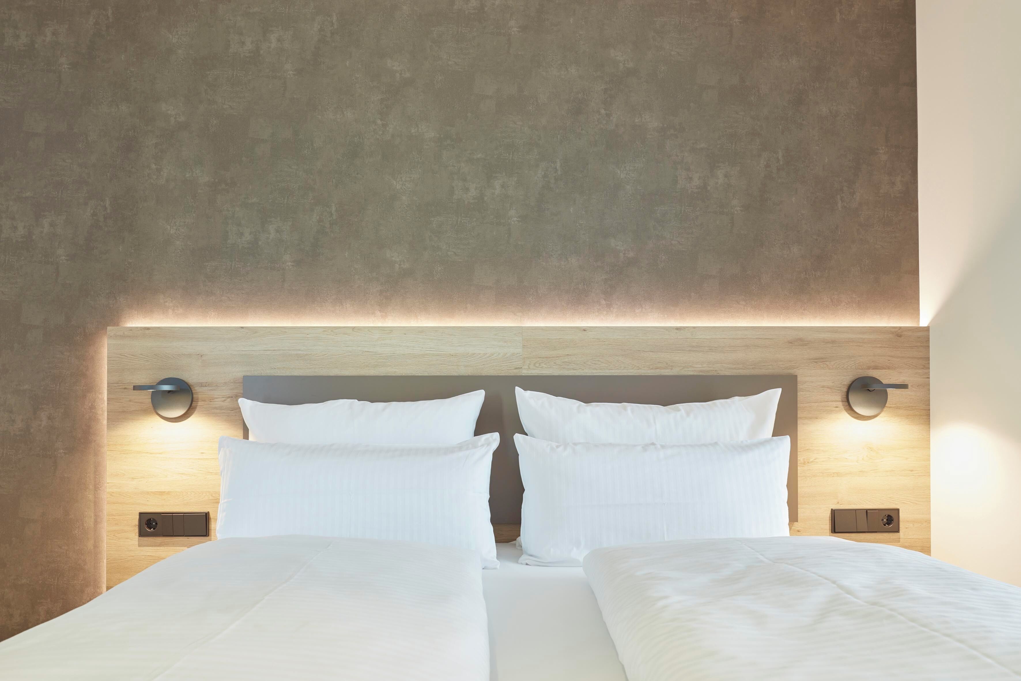 A double bed with white linens, a wooden headboard, and two wall-mounted light fixtures.