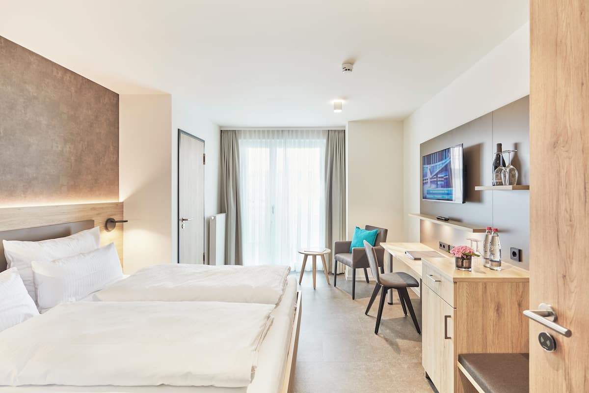 A hotel room with a bed, a desk, a chair, a TV, and a minibar.