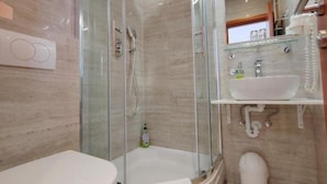 Un baño moderno con ducha de vidrio, un lavamanos blanco y un inodoro.