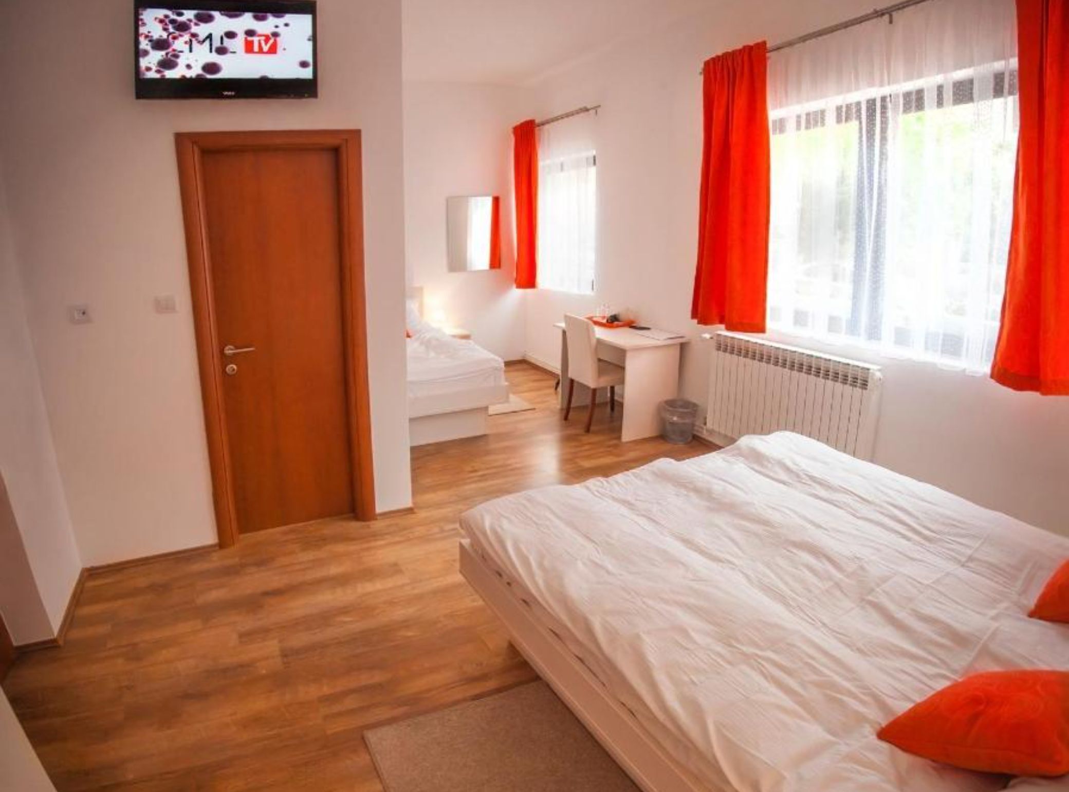A modern bedroom with a wooden door, a bed with white bedding, a desk, and a chair.