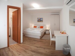 A bedroom with a bed, bedside table, chair, desk, and a trash can. - Rooms Lidija 17 (Zagreb)