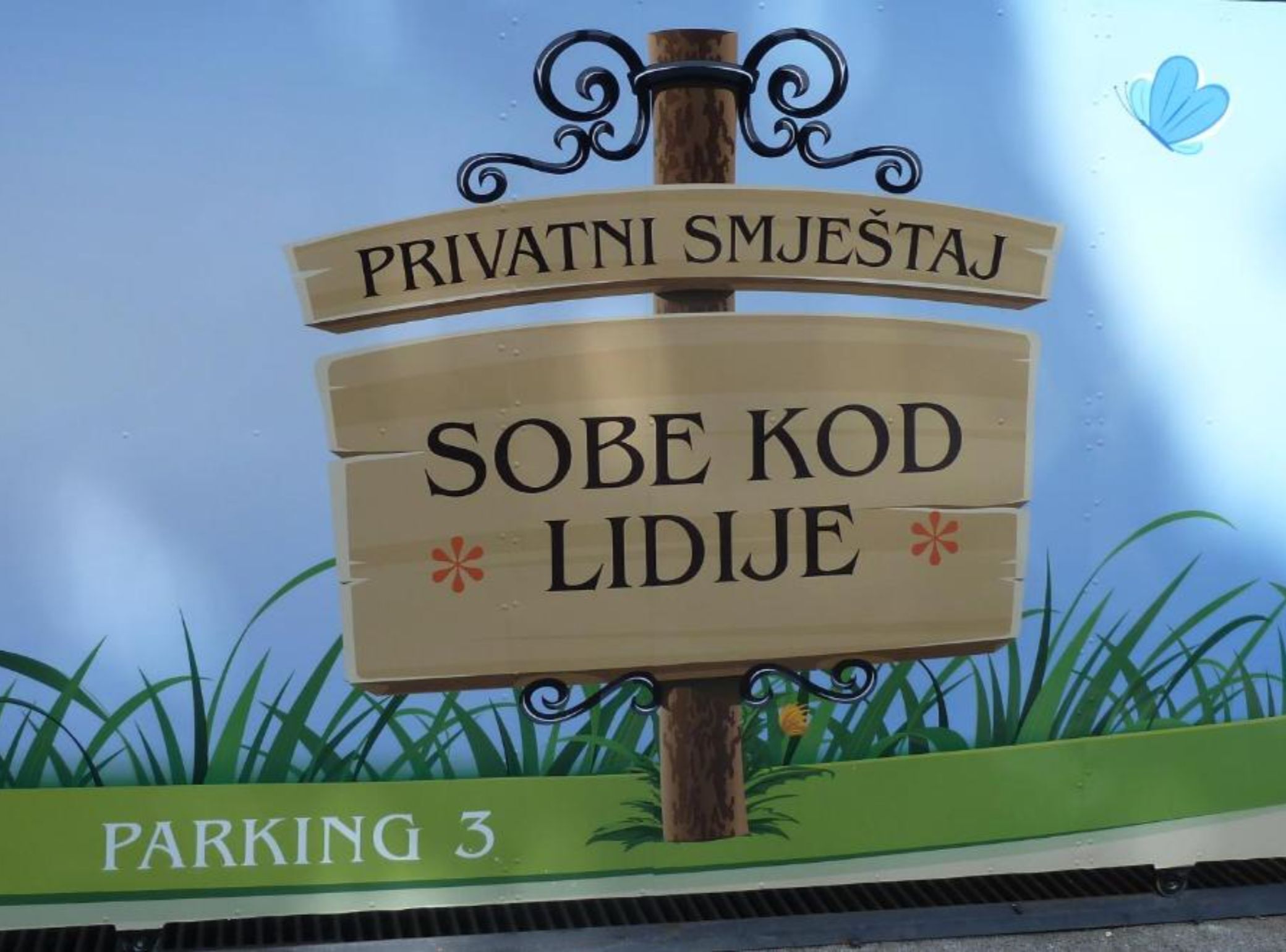 Une pancarte indiquant « PRIVATNI SMJEŠTAJ » et « SOBE KOD LIDJJE », signalant la présence d’un parking privé.
