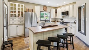 A modern kitchen with white cabinetry, a stainless steel refrigerator, a built-in stove, and a large window.