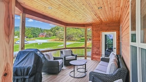 A covered outdoor area with wicker furniture, a grill, and a view of a green landscape.