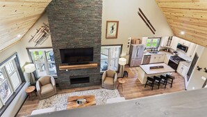 A spacious loft with a stone fireplace, a kitchen with modern appliances, and a dining area with a large window.