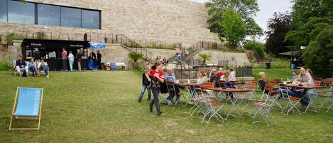 An outdoor seating area with tables and chairs, a stone building in the background, and a signboard.