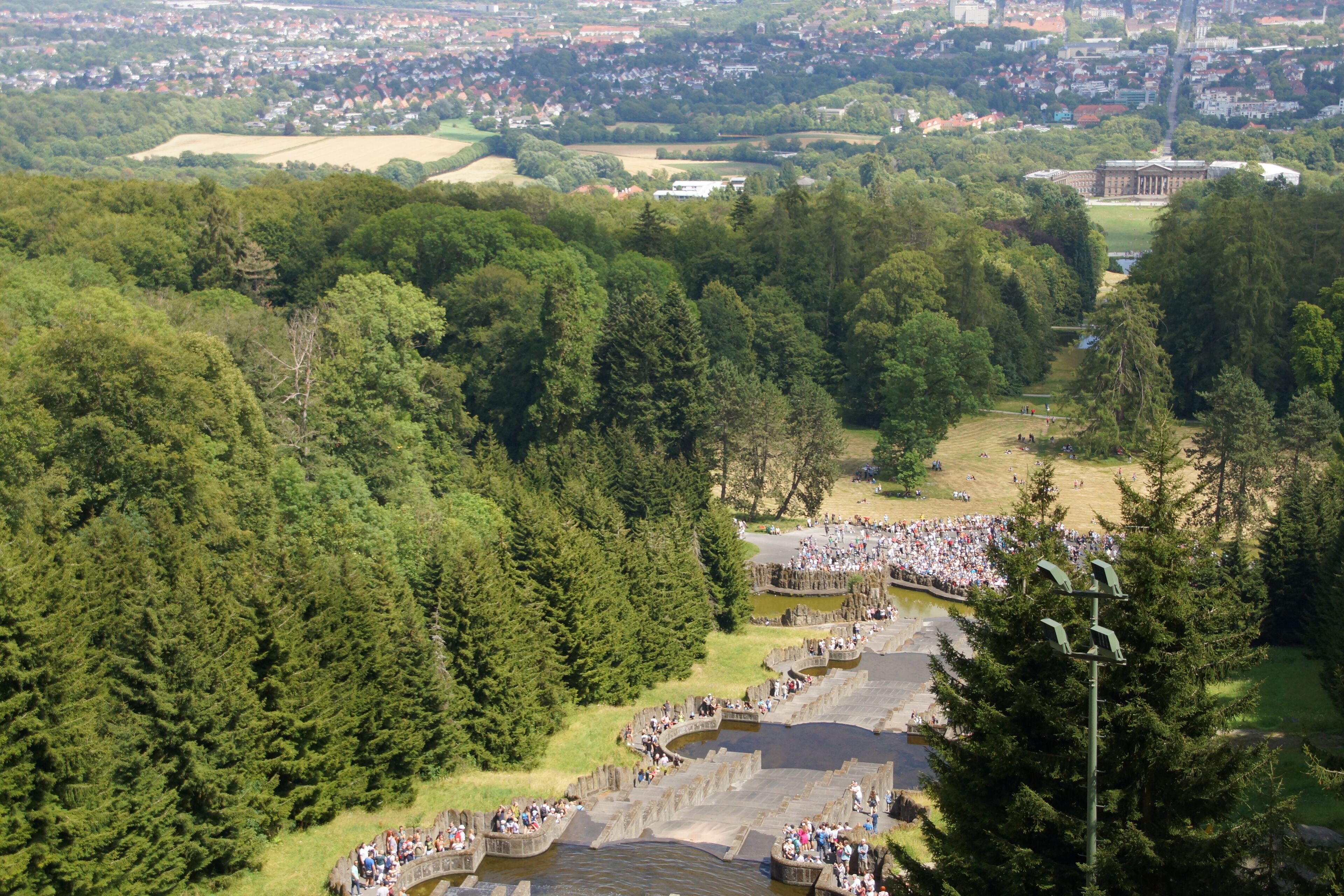 Ein großes, offenes Amphitheater, umgeben von dichtem Wald, mit einer Menge von Menschen zu einer Veranstaltung.