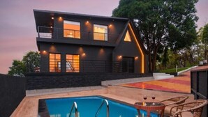 Uma casa moderna com dois andares, piscina, área de estar externa e uma varanda bem iluminada.