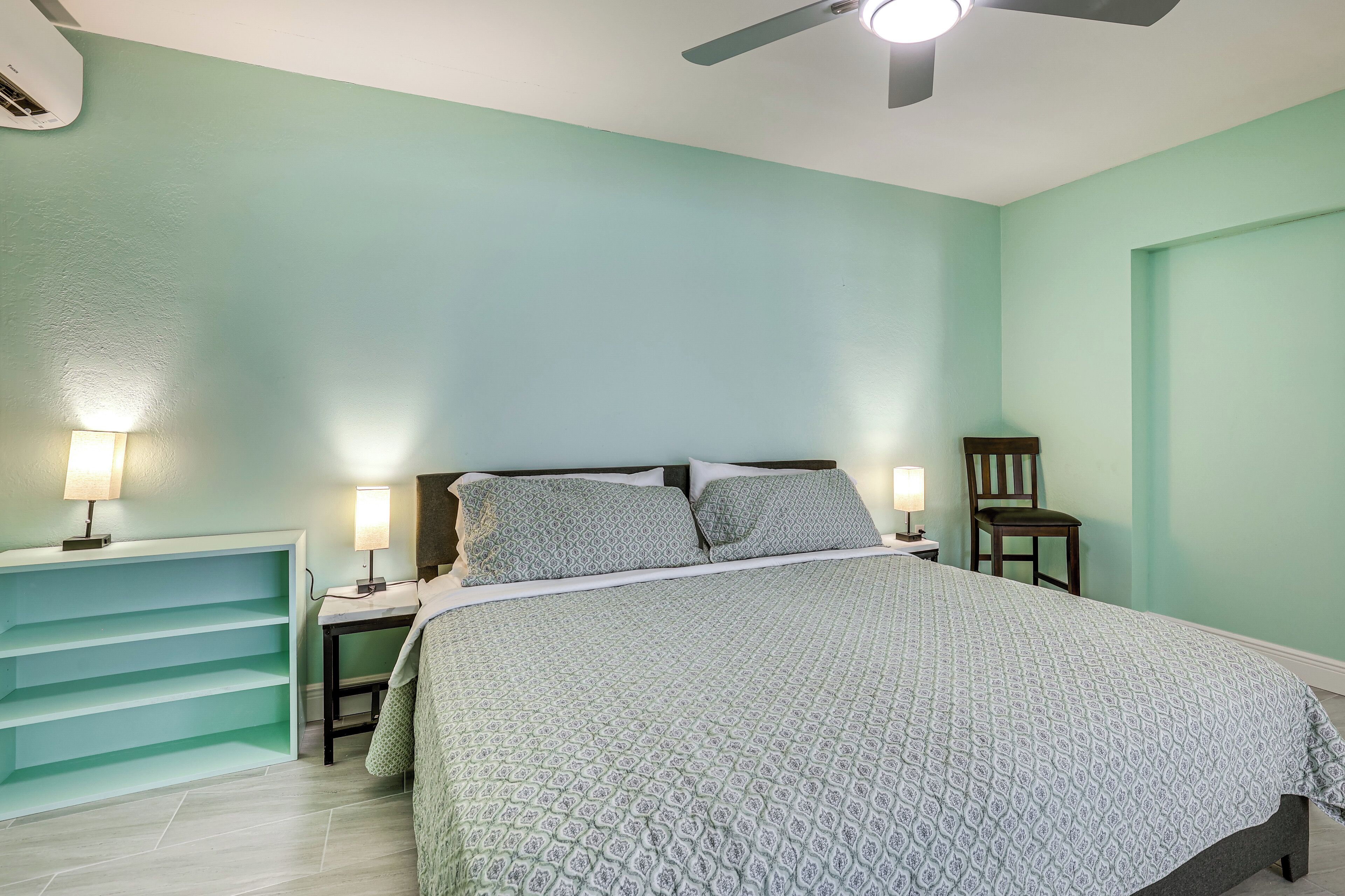 A bedroom with a bed, two bedside lamps, a chair, and a built-in shelving unit.