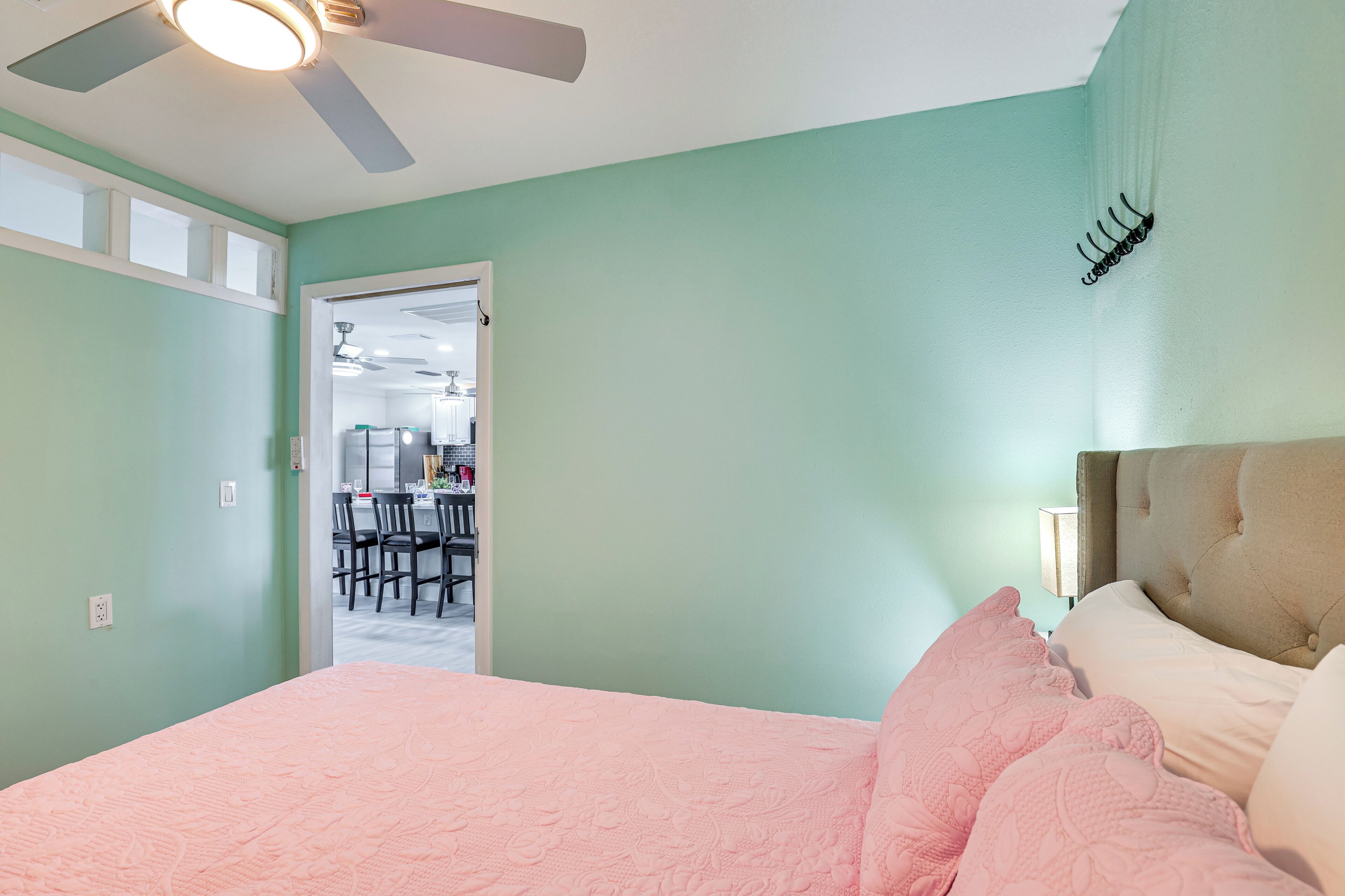 A bedroom with a bed, a ceiling fan, and a door leading to a dining area.