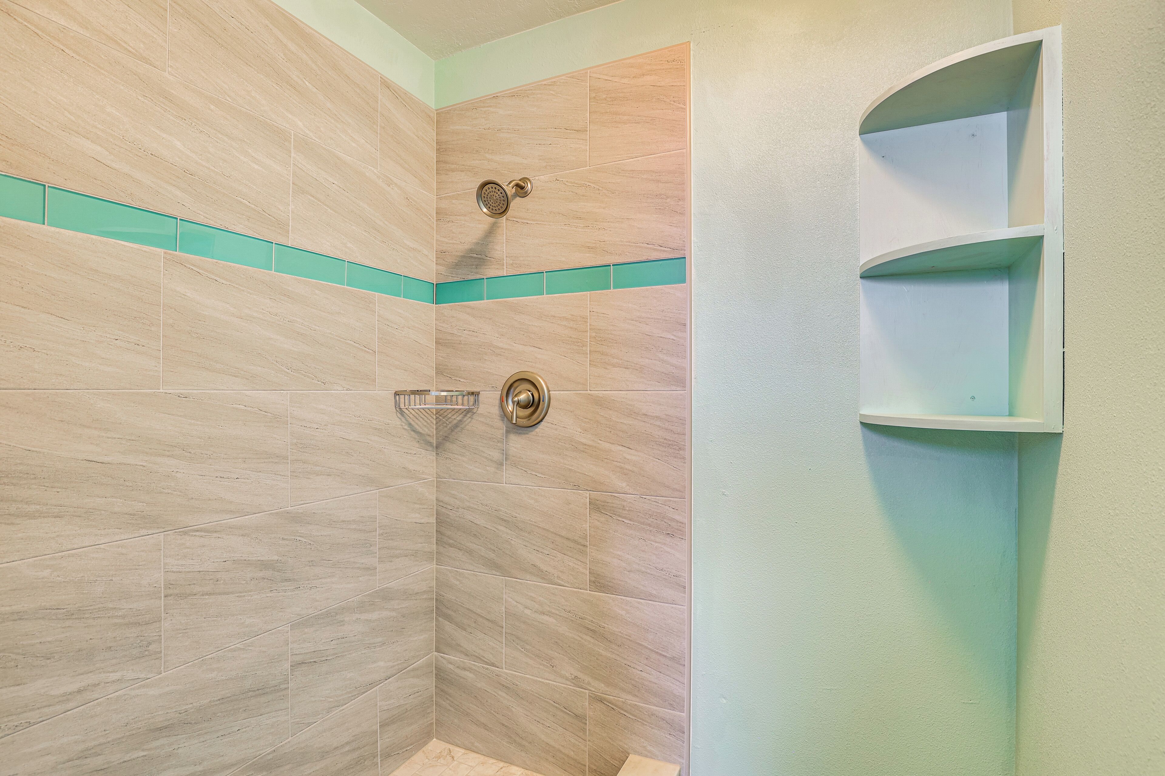 A shower with beige tiles and a teal accent strip.