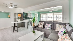 A modern living room with a grey sofa, white coffee table, and a kitchen area with a fridge and dining table. - Ocean View, Pool & Boat Dock: Indian Rocks Retreat (Indian Rocks Beach)
