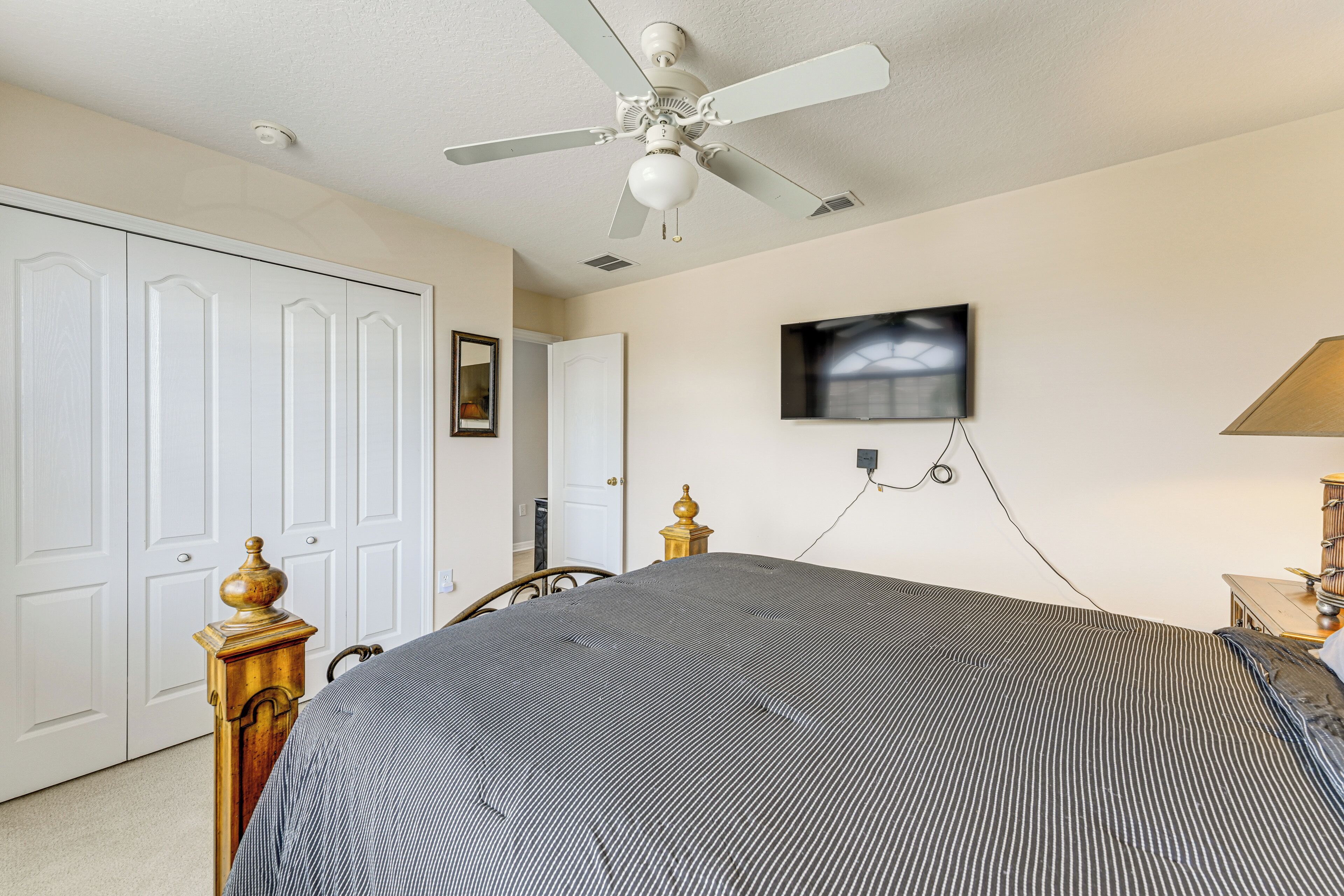 Une chambre à coucher comprenant un lit, un ventilateur de plafond, un téléviseur fixé au mur et une table de chevet avec une lampe.