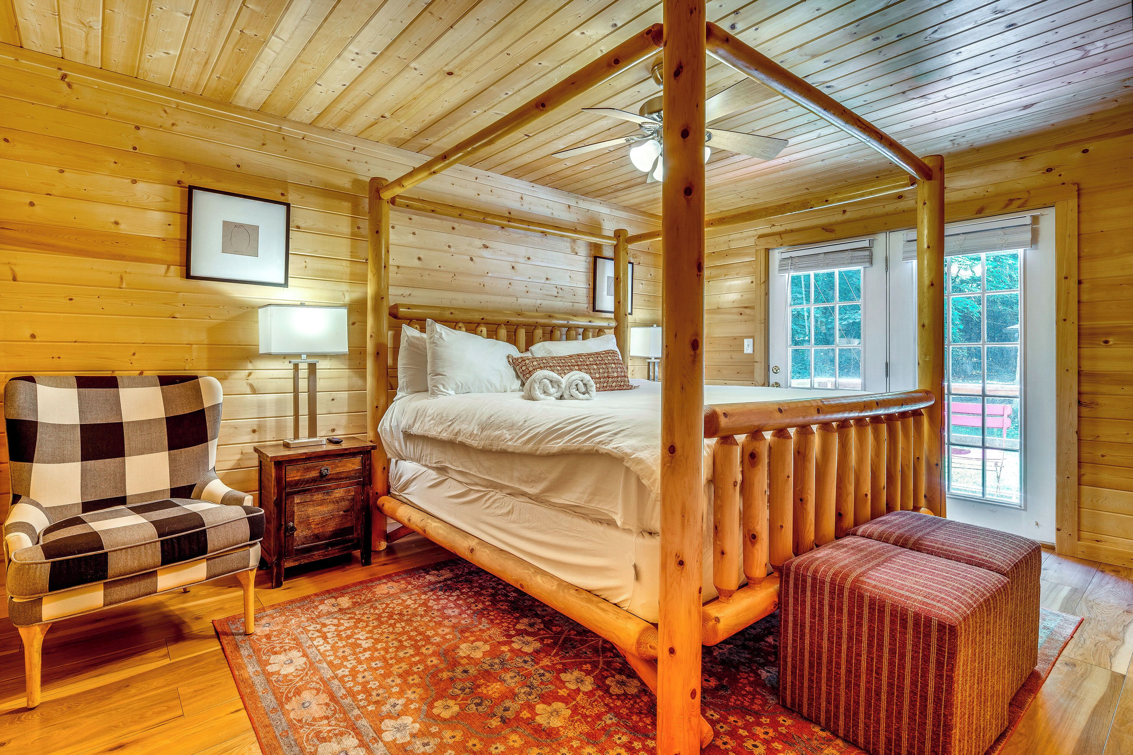 A wooden four-poster bed with a bench and armchair, a small bedside table, and a patterned rug.