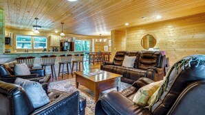 A cozy cabin interior with wooden walls, leather furniture, a dining area, and a kitchen.