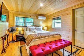 A wooden cabin bedroom with a bed, bedside lamps, a fan, and a bench. - Creekside Smokies Log Cabin w/ Hot Tub & Game Room (Gatlinburg)
