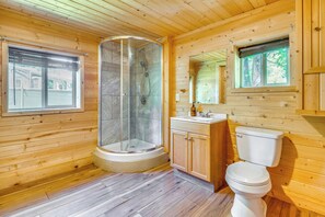 Ein Badezimmer einer Holzhütte mit einer Glasdusche, Holzschränken und einer Toilette.
