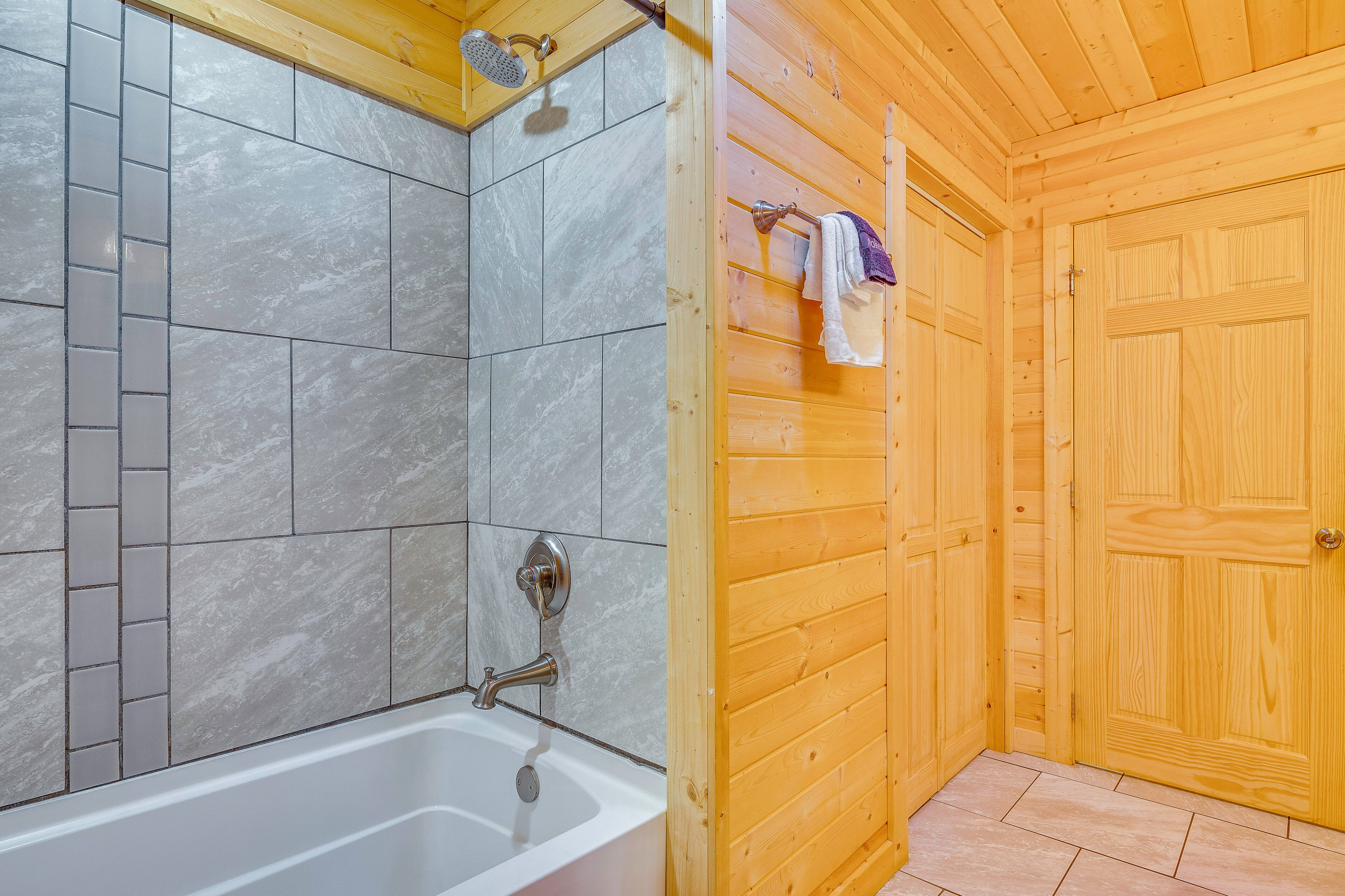 A wooden cabin interior with a shower area featuring grey tiles and a white bathtub.