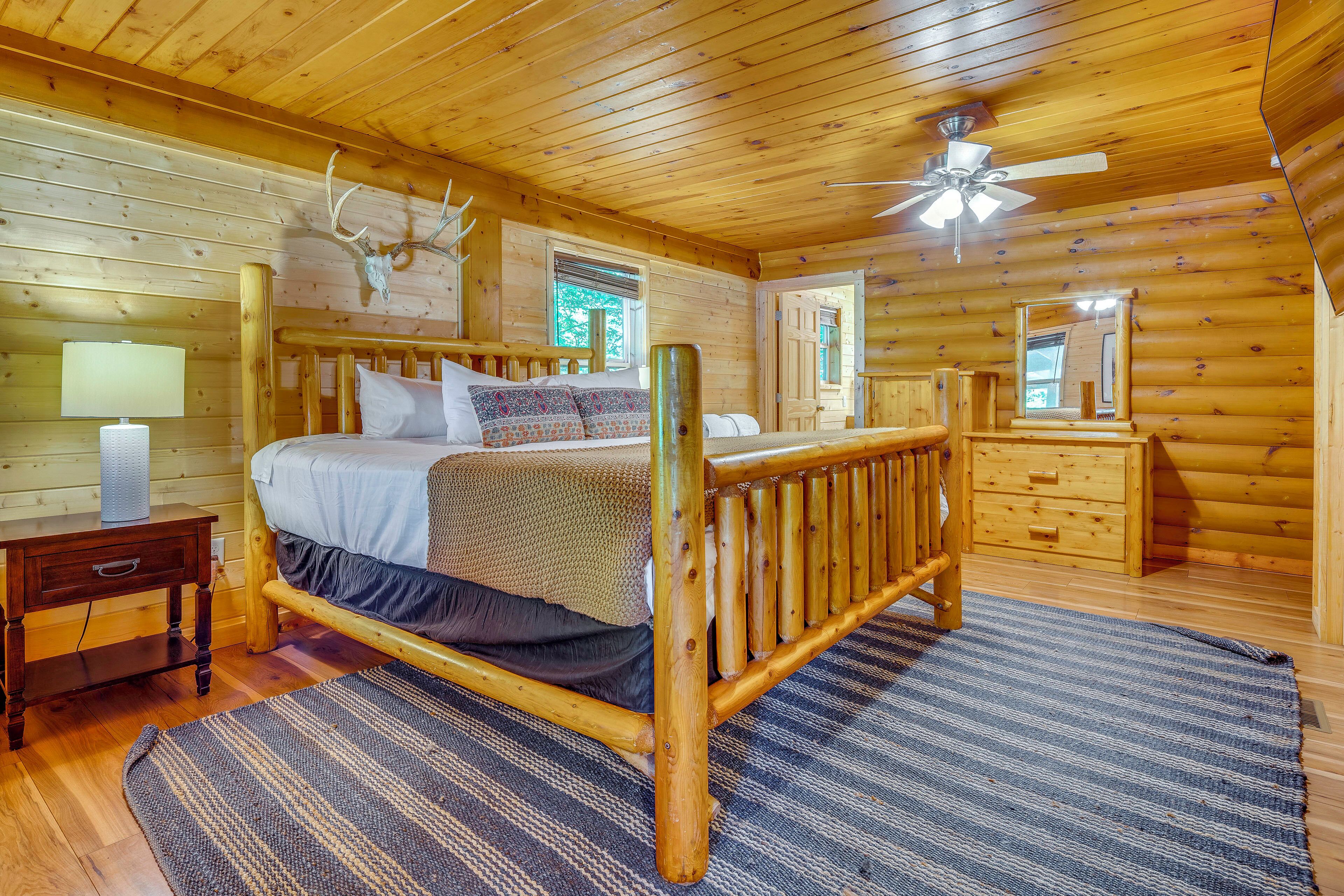 A wooden cabin bedroom with a bed, nightstand, dresser, and a ceiling fan.