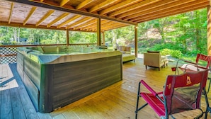 A wooden deck with a hot tub, outdoor furniture, and a view of a forested area.