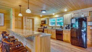 A wooden cabin interior with a kitchen island, bar stools, wooden cabinets, and a stainless steel refrigerator.