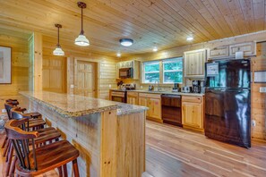 Ein Holzblockhaus-Interieur mit Kücheninsel, Barhocker, Holzschränken und einem Edelstahlkühlschrank.