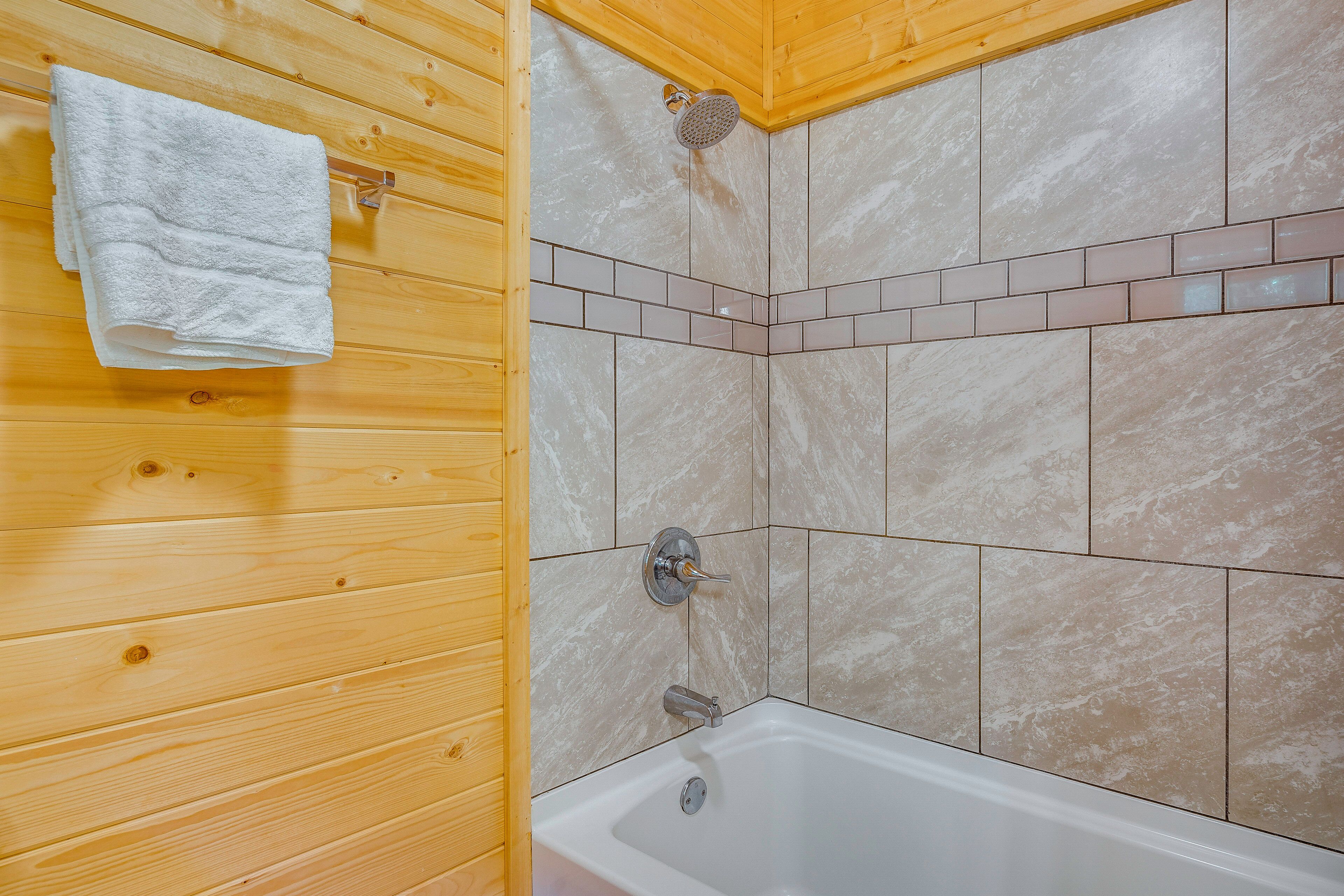 Une salle de bain aux murs lambrissés, équipée d’une baignoire, d’une pomme de douche et d’un espace de douche carrelé.