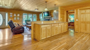 A wooden cabin interior with a kitchen island, wooden flooring, and a fireplace.